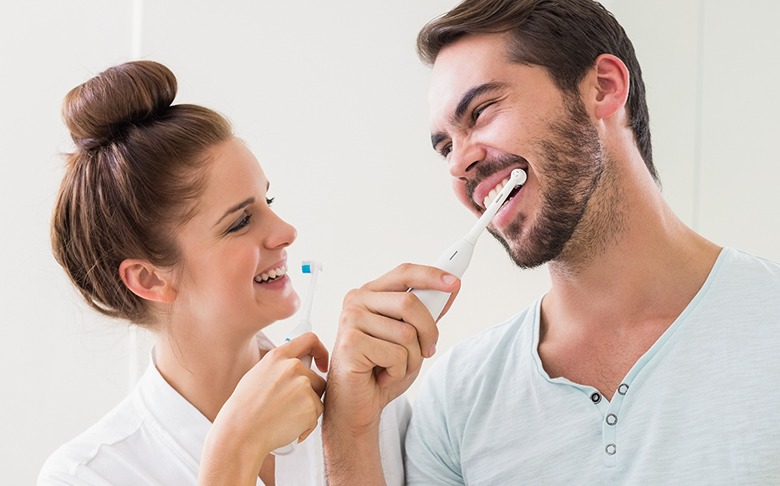 A woman and man playfully brush their teeth together, showcasing dental hygiene. The scene highlights a fun, shared experience promoting oral health.